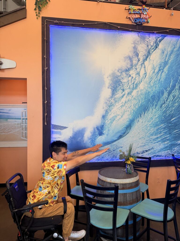 Mike posing with his arms out in front of a giant crashing wave photo backdrop