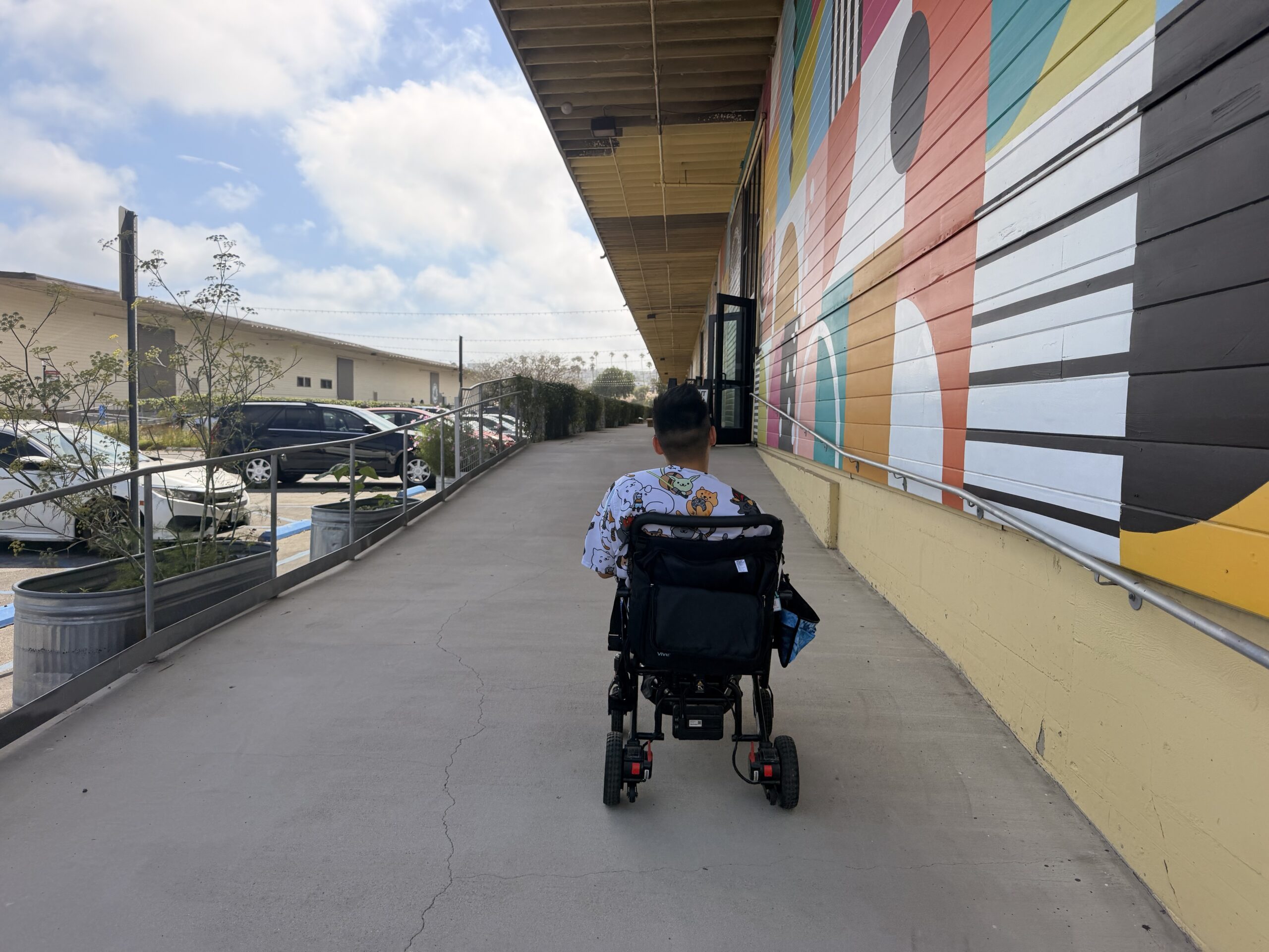 Mike rolling down a long sidewalk beside a geometric mural
