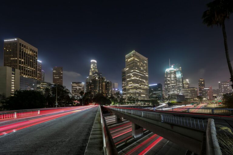 Downtown Los Angeles skyscrapers at night, with headlight trails running along the freeway below.