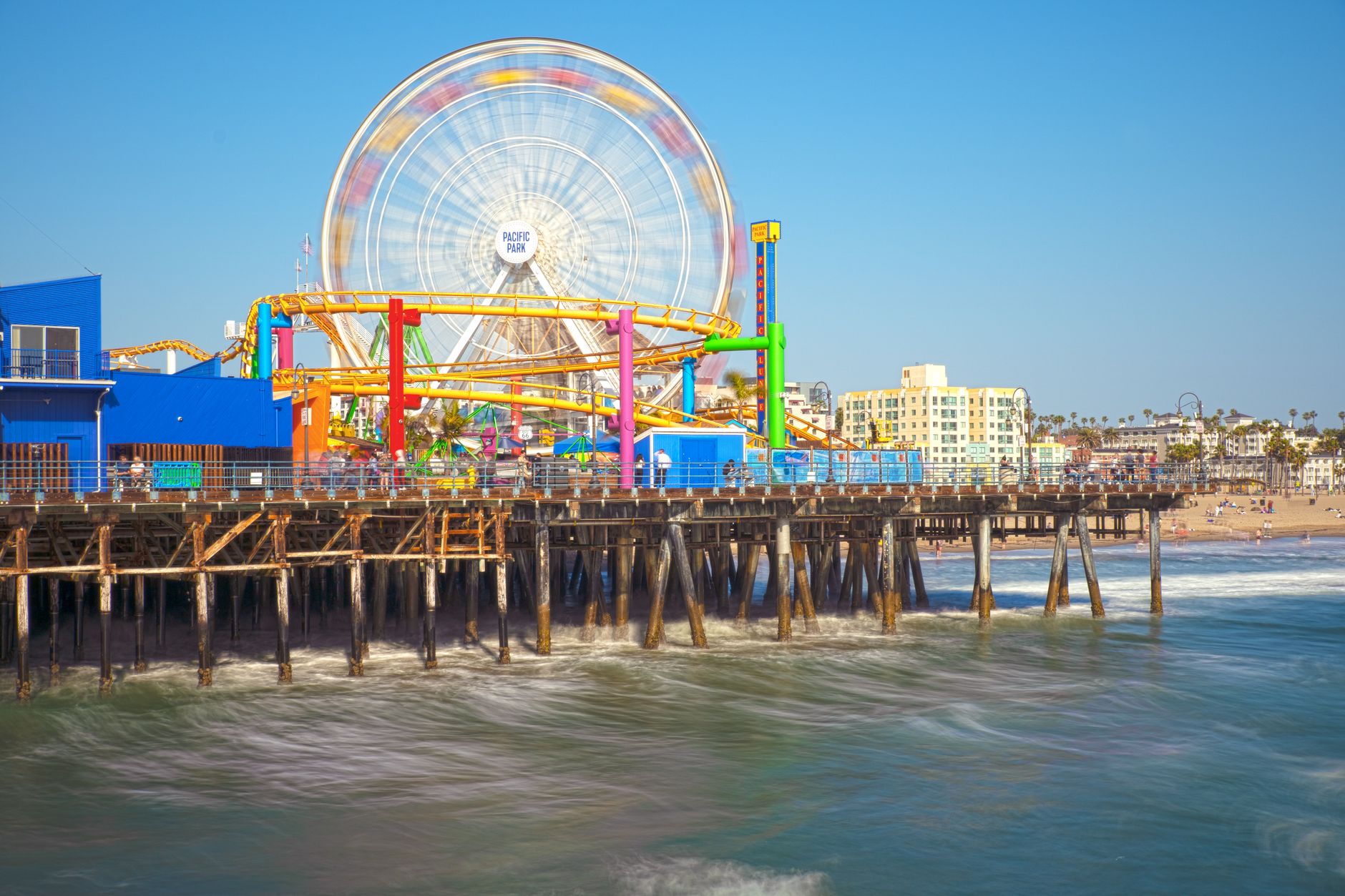 Santa Monica Pier seen from the water, with Pacific Park rides above the wooden pilings.