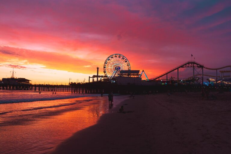 Santa Monica Pier at sunset, with the Ferris wheel and roller coaster lit against a pink sky.