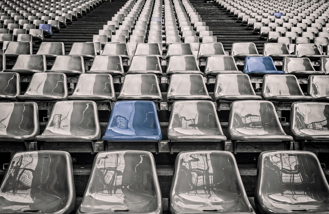 Rows of empty plastic grandstand seats in a stadium, with one blue seat among the gray.