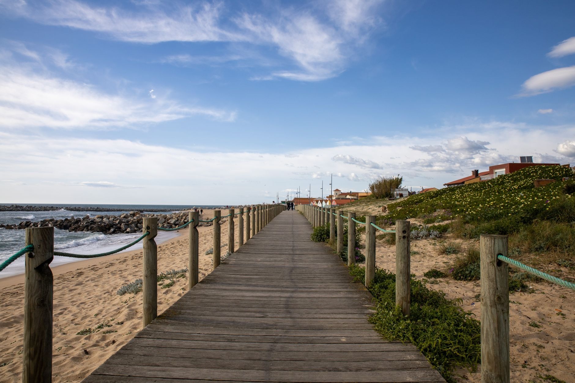 A wooden boardwalk running straight through low dunes toward the ocean