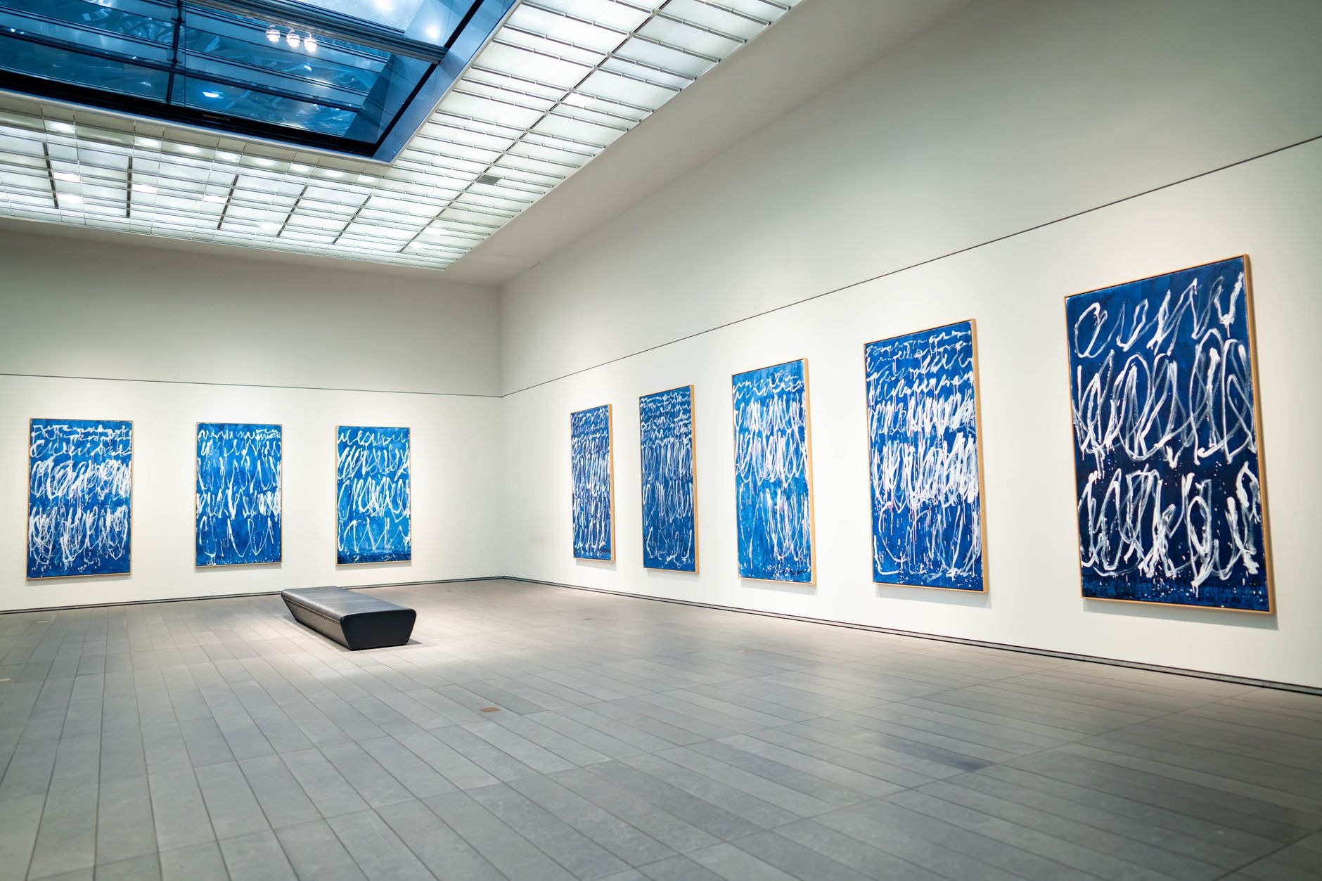 A white-walled contemporary art gallery hung with blue abstract paintings above a wide concrete floor