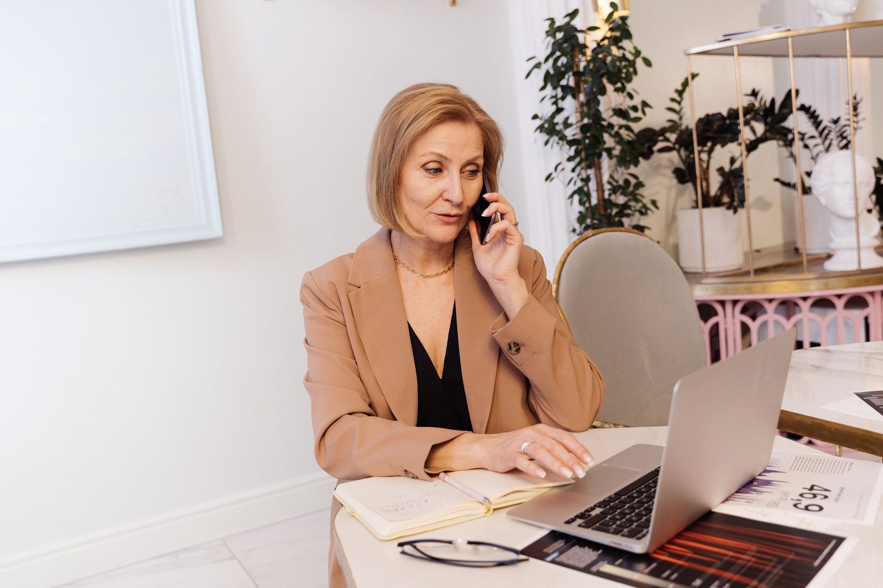 A woman sitting at a desk making a phone call with a laptop and notepad in front of her