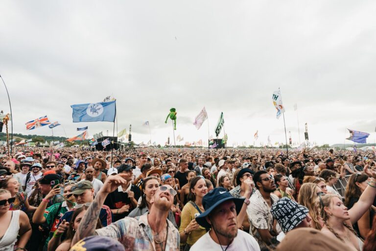 A large daytime festival crowd standing on a field with flags raised above the audience