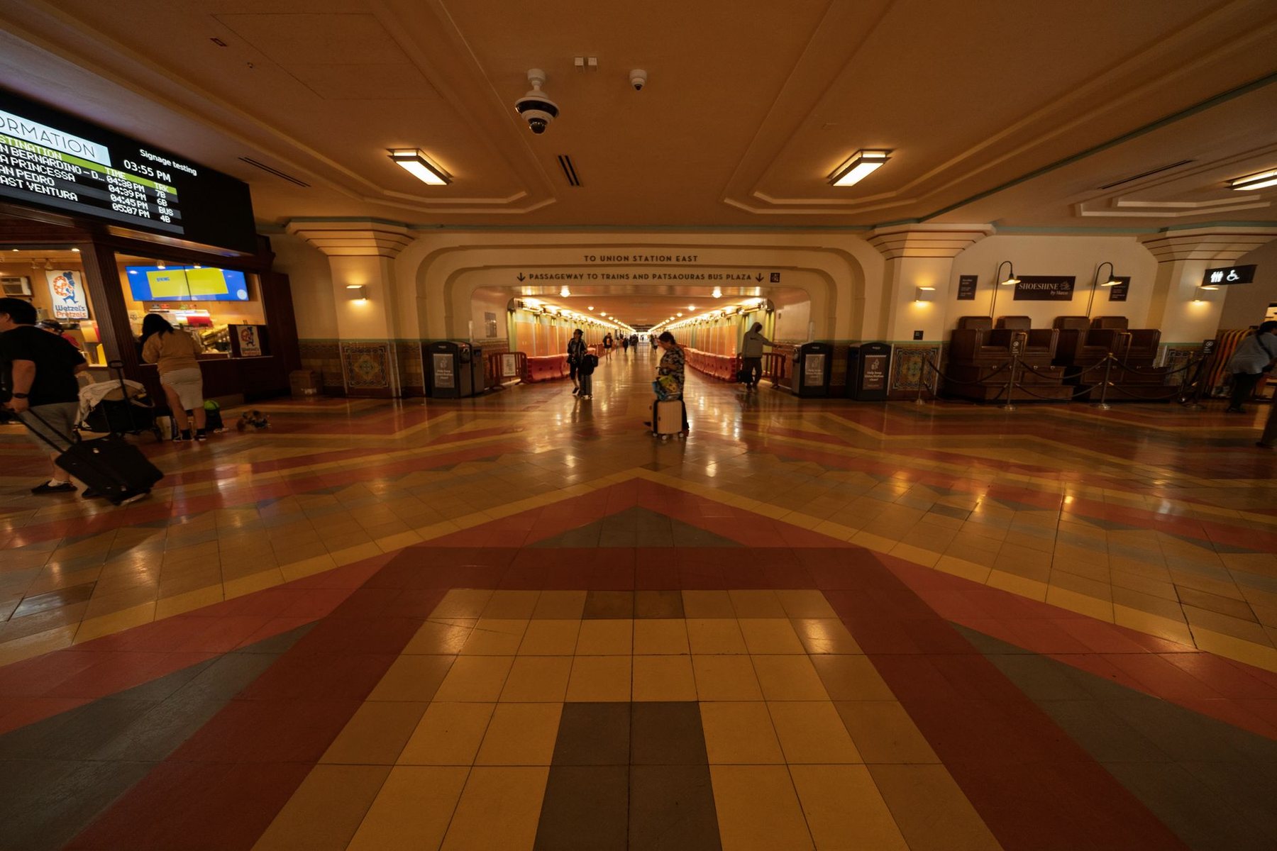 The main concourse of a train station, with a patterned tile floor and a departure board above the doorways