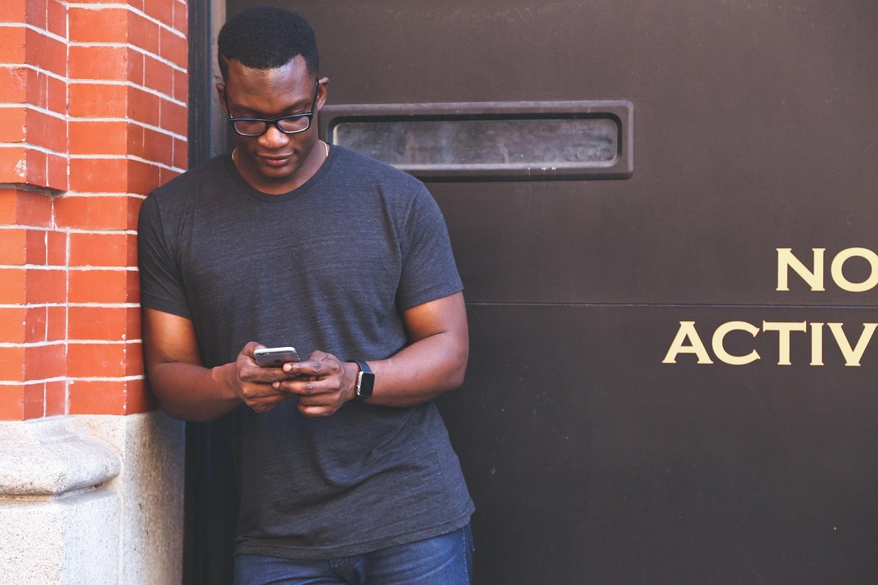 A man standing against a brick wall outside a building, checking his phone