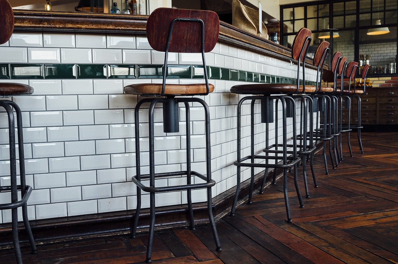 Tall bar stools with backrests lined up along a high tiled bar counter