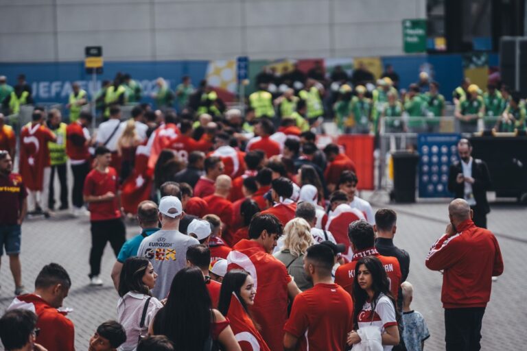 A large crowd of fans in red waiting in line outside a stadium entrance
